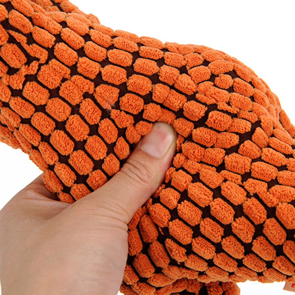 Close-up of the orange Jurassic Chew dinosaur dog toy's belly being squeezed, showcasing its soft corn velvet texture and resilient PP cotton stuffing. White background.